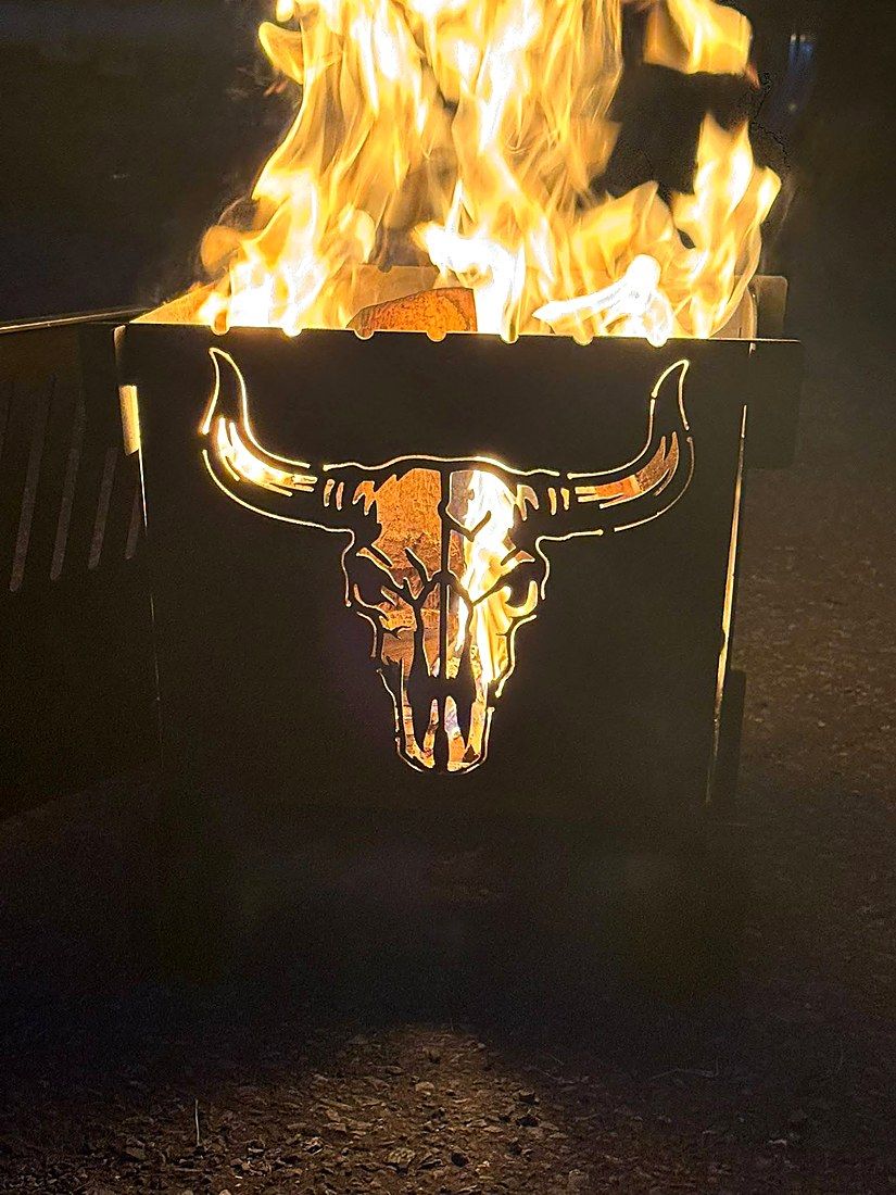 Longhorn skull fire pit lit after dark, flames rising